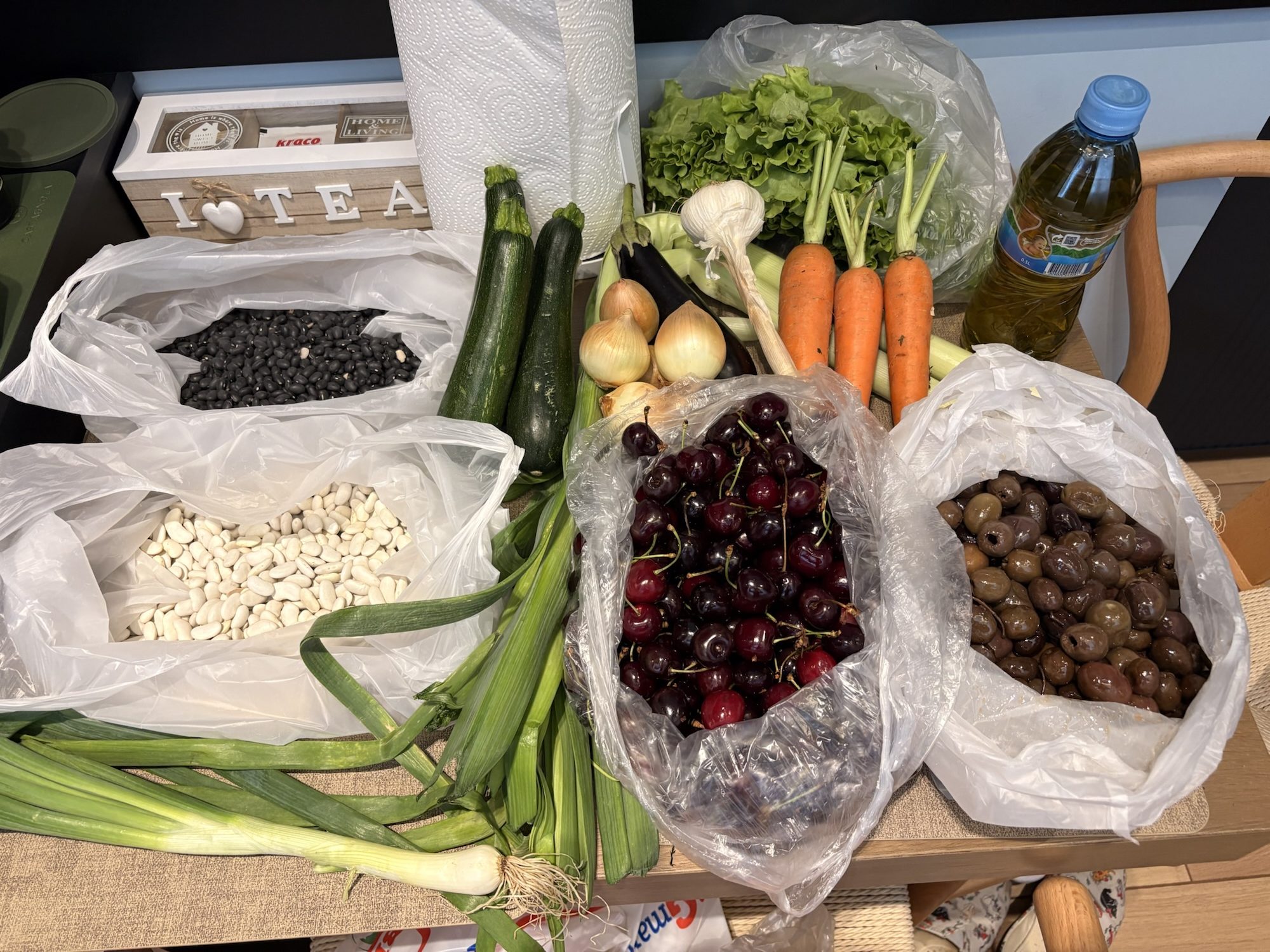 Fresh market haul including cherries, olives, beans, onions, lettuce, carrots, zucchini, and herbs purchased in Albania
